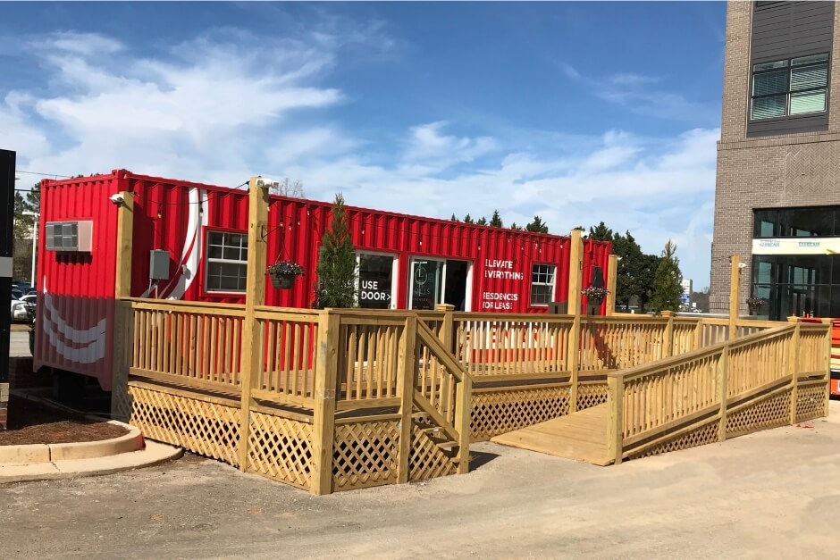 red modified shipping container leasing office with wooden deck next to an apartment building