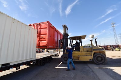worker guides shipping container bathroom onto truck bed