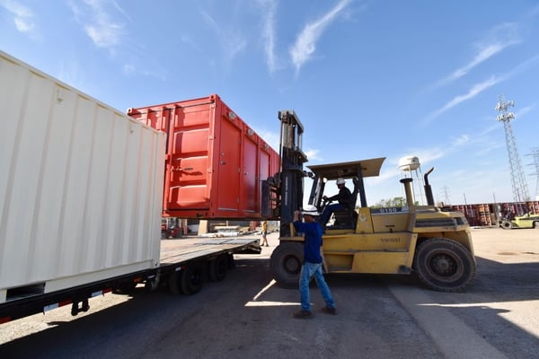 worker guides shipping container bathroom onto truck bed