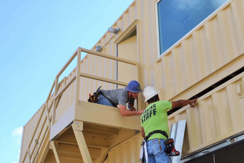 two men assembling two stacked shipping containers with stairs