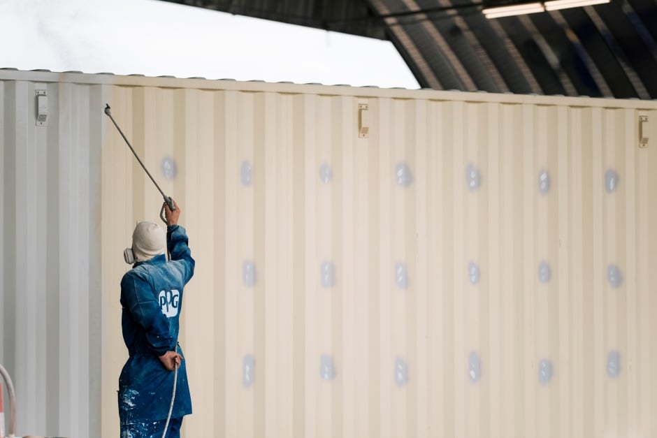 man spray painting a shipping container grey 