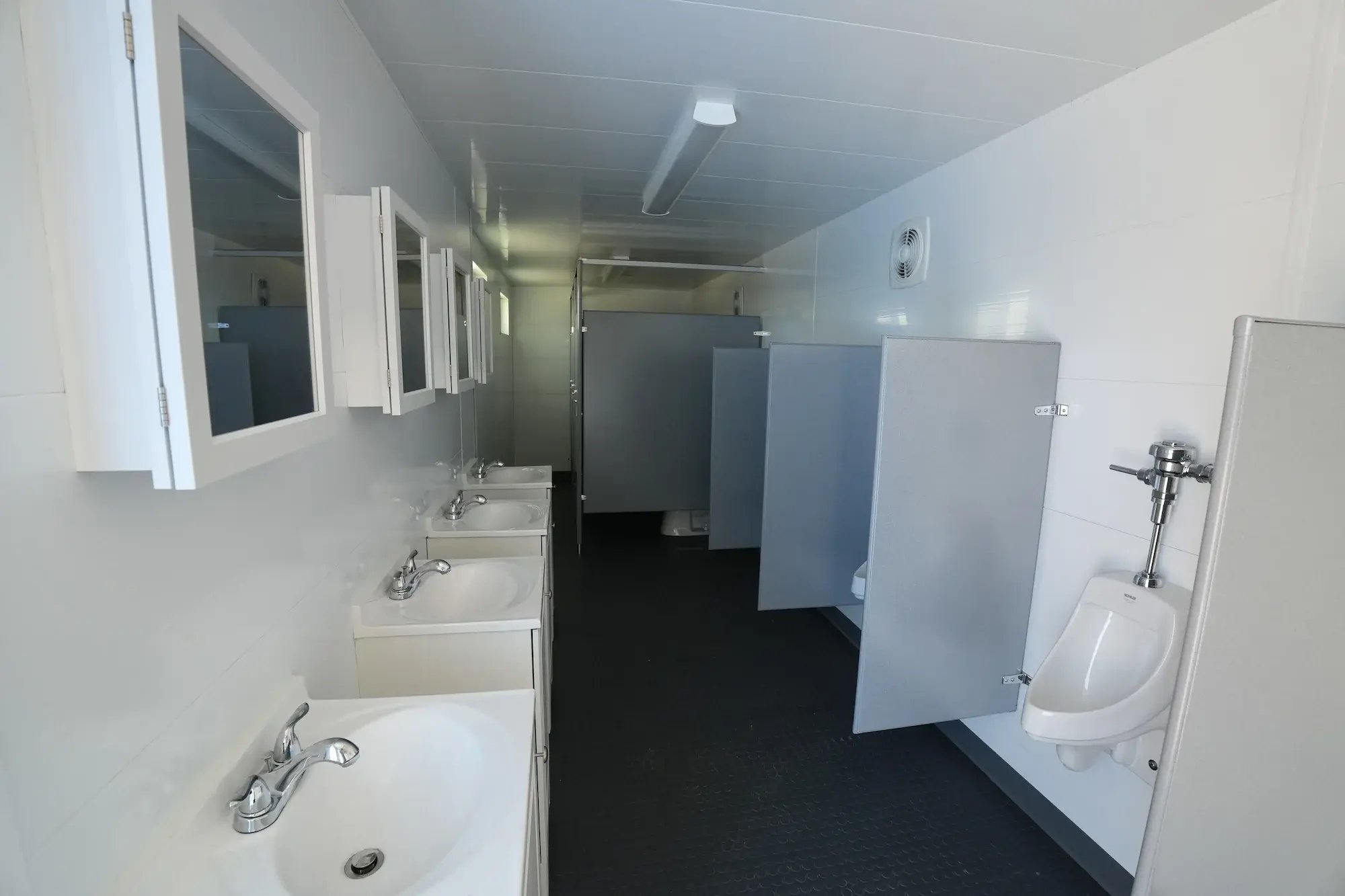 Interior photo of men's bathroom with sinks, urinals, stalls, pvc walls, and privacy windows