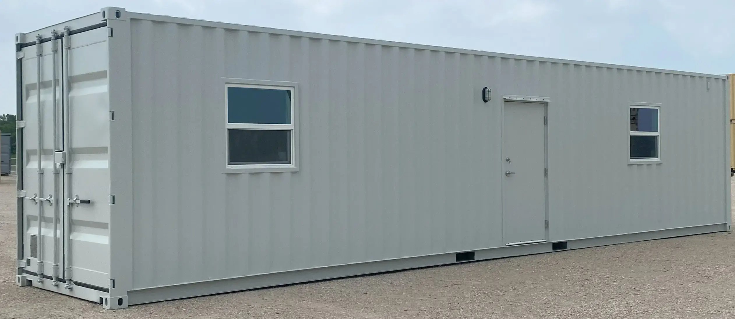 White_shipping_container_with_two_windows_and_a_door_on_gravel_lot