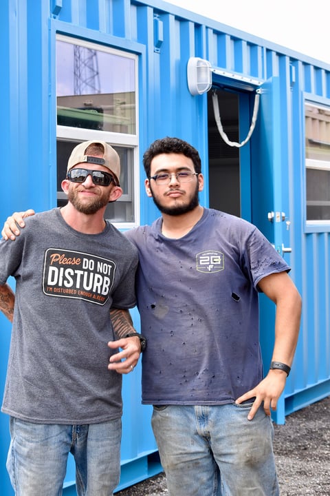 two_men_in_front_of_blue_container.jpeg